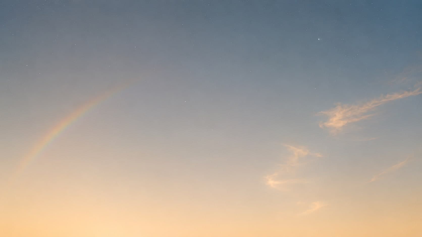 A wide dawn sky, a faint band of rainbow at the left and thin cloud drifting through the light
